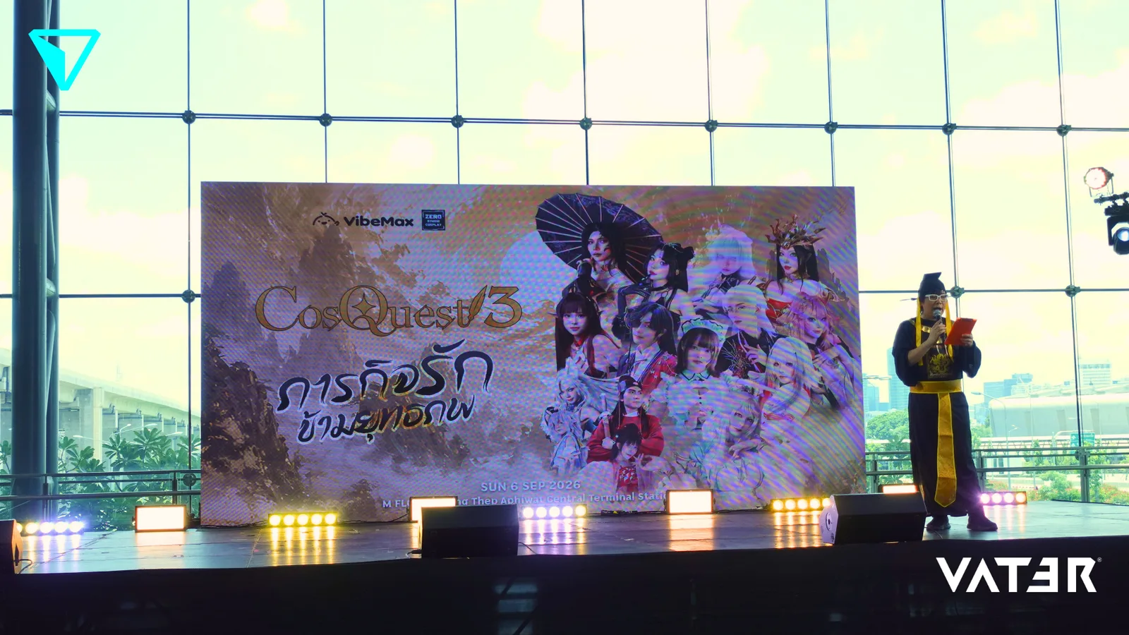 พิธีกรในชุดจีนโบราณยืนพูดบนเวทีข้างจอภาพขนาดใหญ่ของงาน CosQuest 3