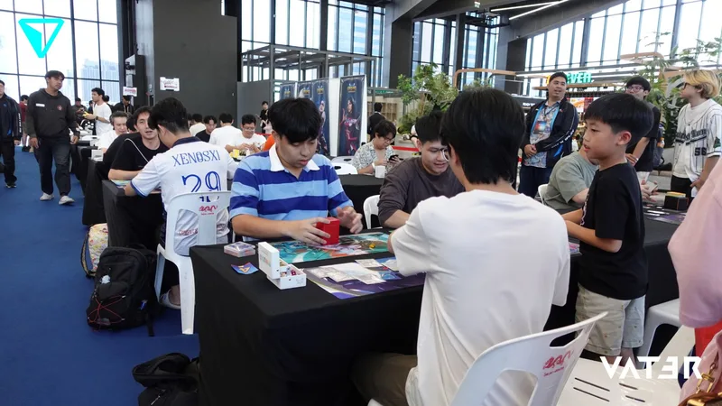 ผู้คนกำลังนั่งเล่นการ์ดเกมประชันกันที่โต๊ะระหว่างการแข่งขันเกมภายในอาคาร