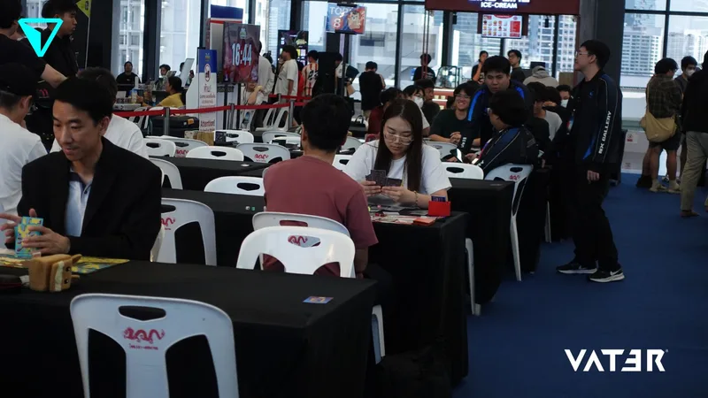 ผู้คนนั่งประจันหน้ากันที่โต๊ะเพื่อเล่นการ์ดเกมในงานแข่งขันทัวร์นาเมนต์เกมในร่มที่มีผู้เข้าร่วมคับคั่ง