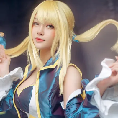 คอสเพลเยอร์แต่งกายเป็น Lucy Heartfilia จาก Fairy Tail สวมวิกผมทวินเทลสีบลอนด์และชุดสีน้ำเงินขาว กำลังจับผมโพสท่ามองกล้อง