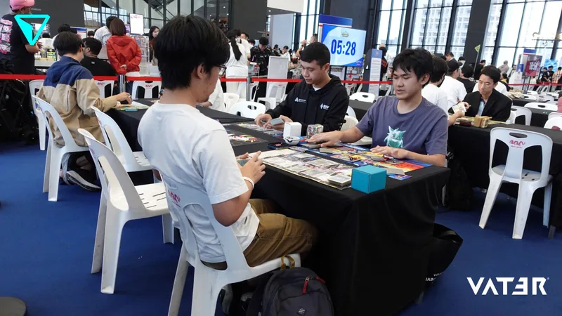 ผู้เข้าแข่งขันกำลังนั่งเล่นการ์ดเกมประลองฝีมือกันที่โต๊ะในงานทัวร์นาเมนต์ที่มีผู้คนคับคั่ง