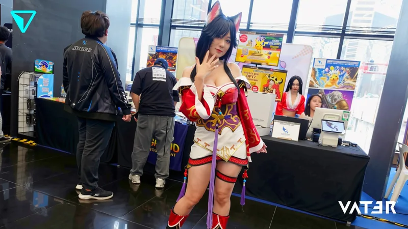 หญิงสาวแต่งคอสเพลย์เป็น Ahri จาก League of Legends สวมชุดสีแดงขาวและหูจิ้งจอก โพสท่าภายในงานเกม