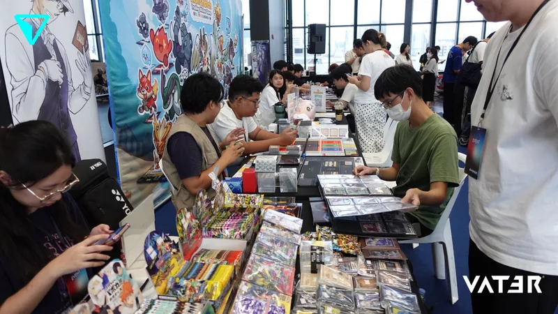 ผู้เข้าร่วมงานกำลังเปิดดูสมุดสะสมการ์ดและสินค้าเกมบนโต๊ะที่จัดแสดงในงานอนิเมะในร่ม