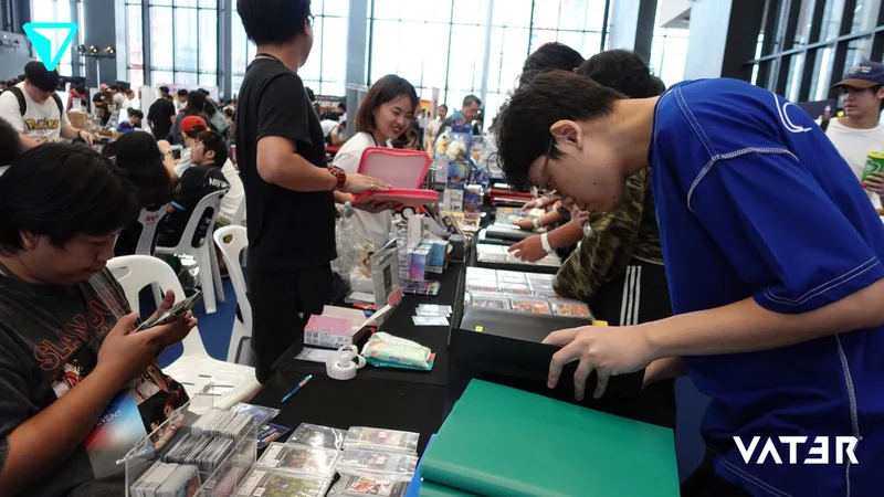 ผู้เข้าร่วมงานกำลังเลือกดูการ์ดสะสมและสินค้าตามโต๊ะจำหน่ายในศูนย์จัดแสดงที่มีผู้คนพลุกพล่าน