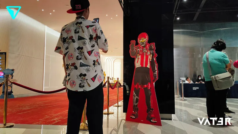 คนสวมเสื้อเชิ้ตมีลายกำลังถ่ายรูปสแตนดี้ตัวละครซูเปอร์ฮีโร่สีแดงใกล้กับทางเดินพรมแดง