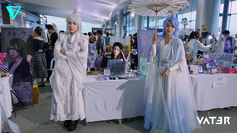 คอสเพลเยอร์สองคนในชุดจีนโบราณแนวจีนแฟนตาซีกำลังยืนโพสท่าข้างบูทสินค้าในงานอนิเมะ