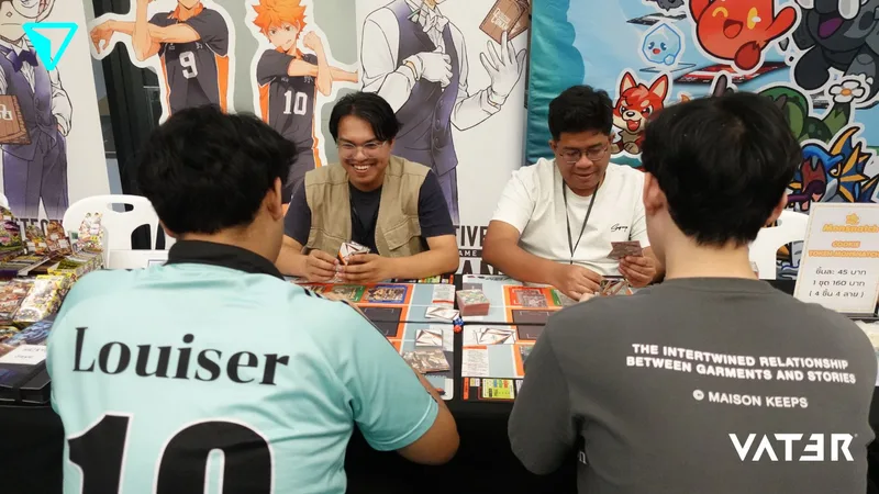ชายหนุ่มสี่คนนั่งเล่นเกมการ์ดข้ามโต๊ะที่บูธในงานการ์ตูนอนิเมะ