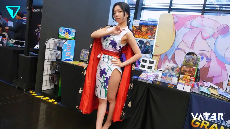 หญิงสาวแต่งคอสเพลย์เป็น Boa Hancock จาก One Piece โพสท่าในชุดเดรสลายดอกไม้ผ่าสูงพร้อมเสื้อคลุมสีแดงที่บูธในงานการ์ตูน