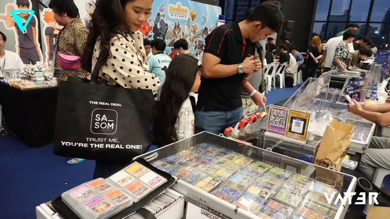 ผู้คนกำลังเลือกชมการ์ดสะสมที่จัดแสดงในตู้กระจกภายในงานมหกรรมเกมและอนิเมะที่คึกคัก