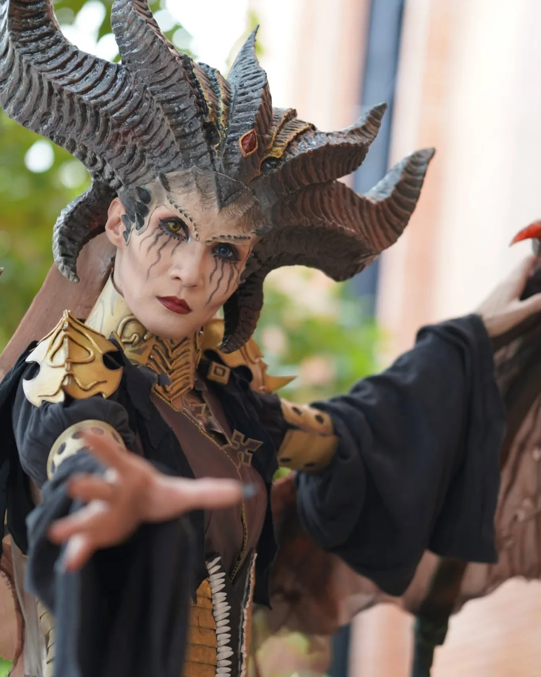 คอสเพลเยอร์แต่งกายเป็น Lilith จาก Diablo IV สวมเครื่องประดับศีรษะมีเขาอันวิจิตรและยื่นมือออกมาข้างหน้า
