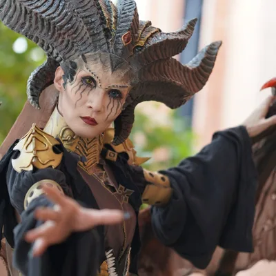 คอสเพลเยอร์แต่งกายเป็น Lilith จาก Diablo IV สวมเครื่องประดับศีรษะมีเขาอันวิจิตรและยื่นมือออกมาข้างหน้า
