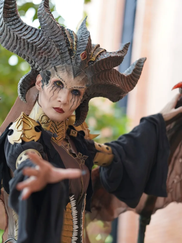 คอสเพลเยอร์แต่งกายเป็น Lilith จาก Diablo IV สวมเครื่องประดับศีรษะมีเขาอันวิจิตรและยื่นมือออกมาข้างหน้า