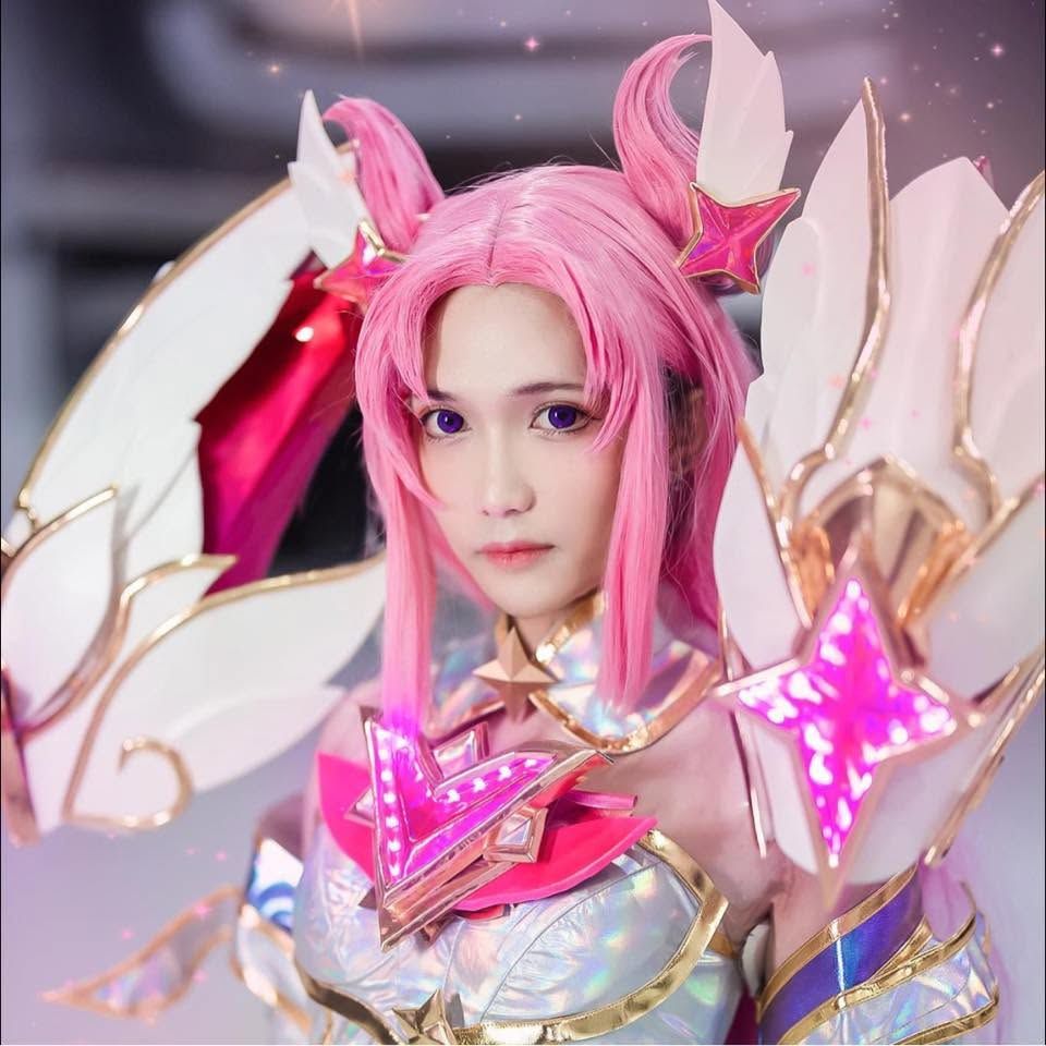 คอสเพลเยอร์ผมสีชมพูโพสท่าในชุด Star Guardian Kai'Sa พร้อมเกราะไหล่ติดปีกขนาดใหญ่และเครื่องประดับรูปดาวสีชมพูเรืองแสง