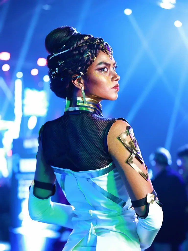 หญิงสาวคอสเพลย์เป็น Mel Medarda จาก Arcane โพสท่าเหลียวมองข้ามไหล่ใต้แสงไฟเวทีสีฟ้าสว่าง