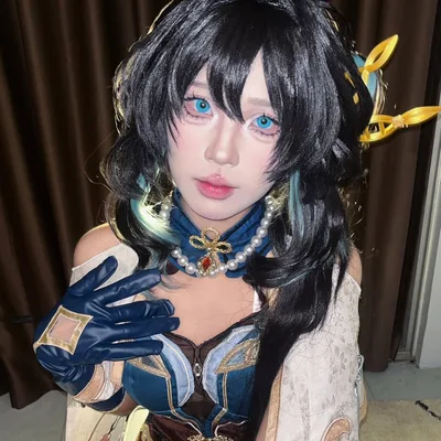 คอสเพลเยอร์แต่งกายเป็น Ruan Mei จาก Honkai: Star Rail โพสท่าในร่มพร้อมคอนแทกต์เลนส์สีฟ้าและวิกผมสีเข้มสไตล์เฉพาะตัว