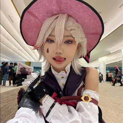 คนคอสเพลย์เป็น Lyney จาก Genshin Impact กำลังแลบลิ้นอย่างขี้เล่นพร้อมถือไพ่ในงานอนิเมะคอนเวนชัน