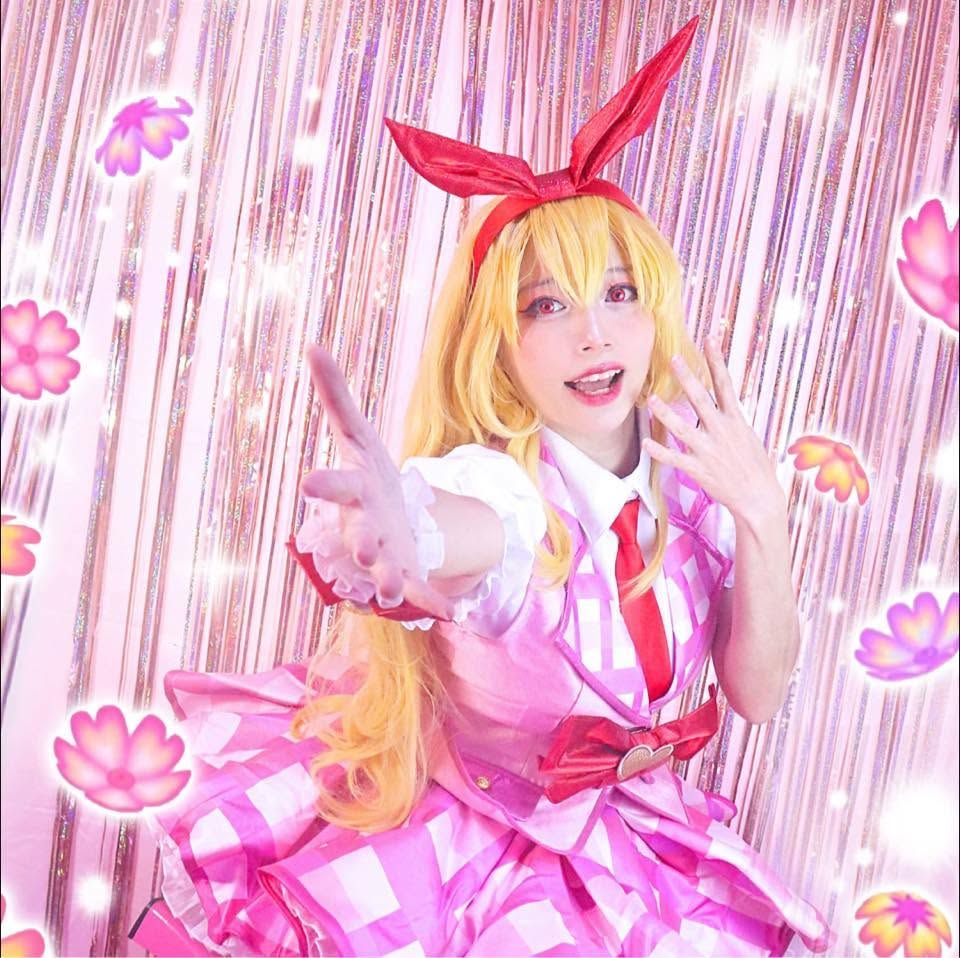 คอสเพลเยอร์ในชุด Ichigo Hoshimiya ยื่นมือมาข้างหน้าหน้าม่านประกายสีชมพูสดใส