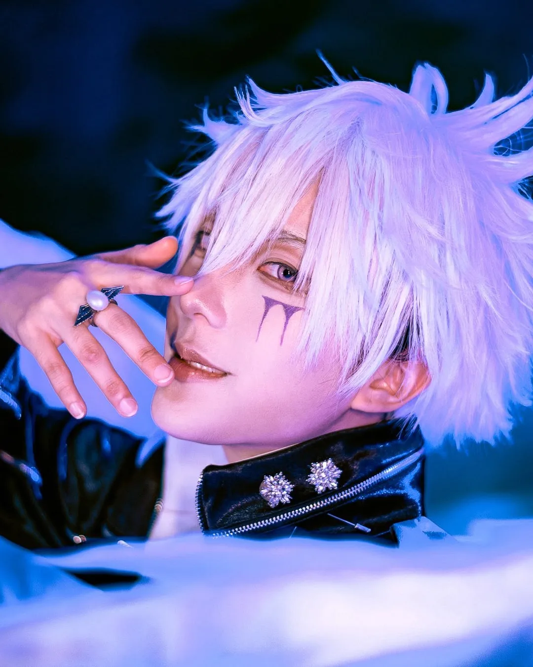 คอสเพลเยอร์ในชุด Byakuran จาก Katekyo Hitman Reborn! โพสท่าท่ามกลางปีกสีขาวและยกมือแตะใบหน้าใต้แสงไฟสีน้ำเงิน