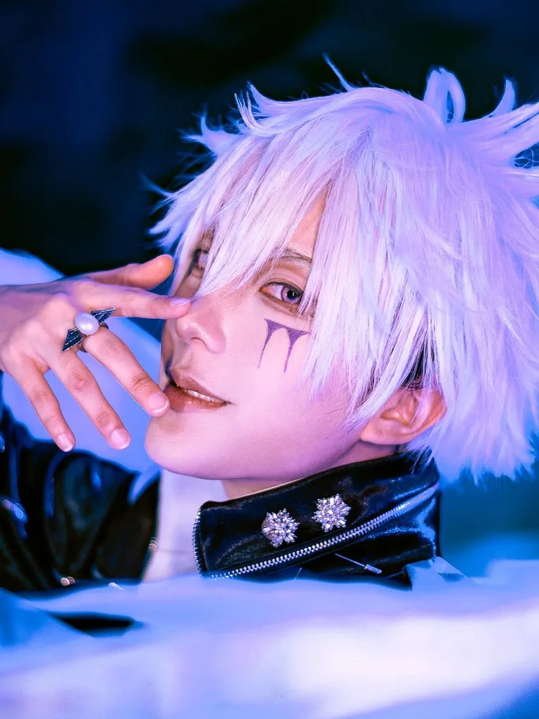 คอสเพลเยอร์ในชุด Byakuran จาก Katekyo Hitman Reborn! โพสท่าท่ามกลางปีกสีขาวและยกมือแตะใบหน้าใต้แสงไฟสีน้ำเงิน
