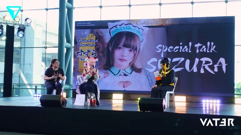 คอสเพลเยอร์ Suzura กำลังพูดคุยบนเวทีกิจกรรมร่วมกับพิธีกรหน้าจอขนาดใหญ่ที่แสดงภาพของเธอ