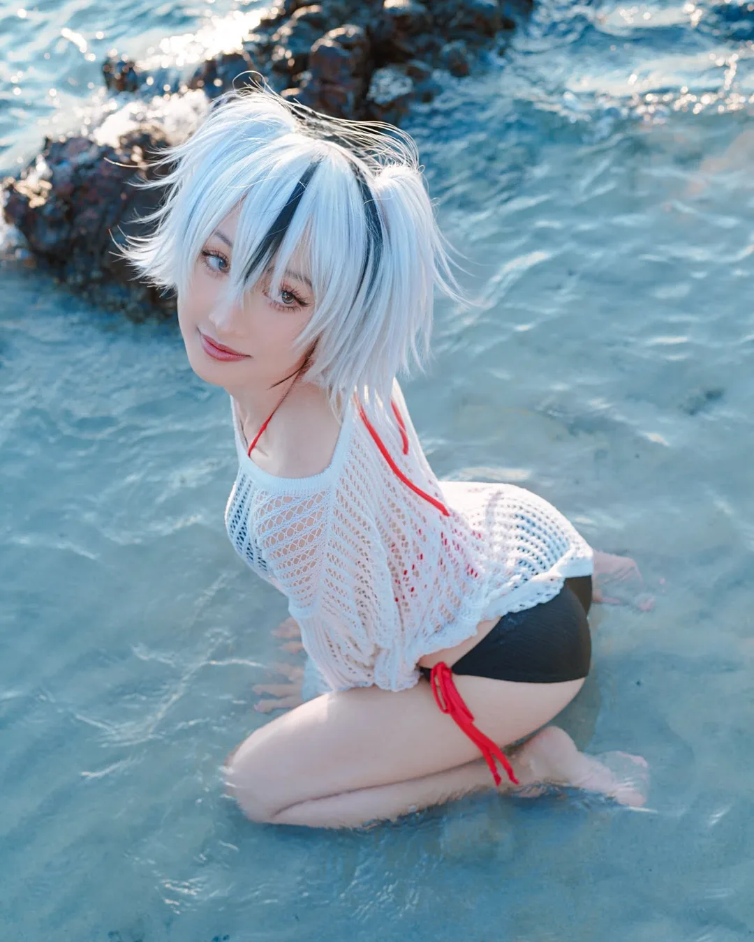 คอสเพลเยอร์ในชุด Summer Jeanne Alter จาก Fate/Grand Order คุกเข่าอยู่ในน้ำทะเลใสริมโขดหิน