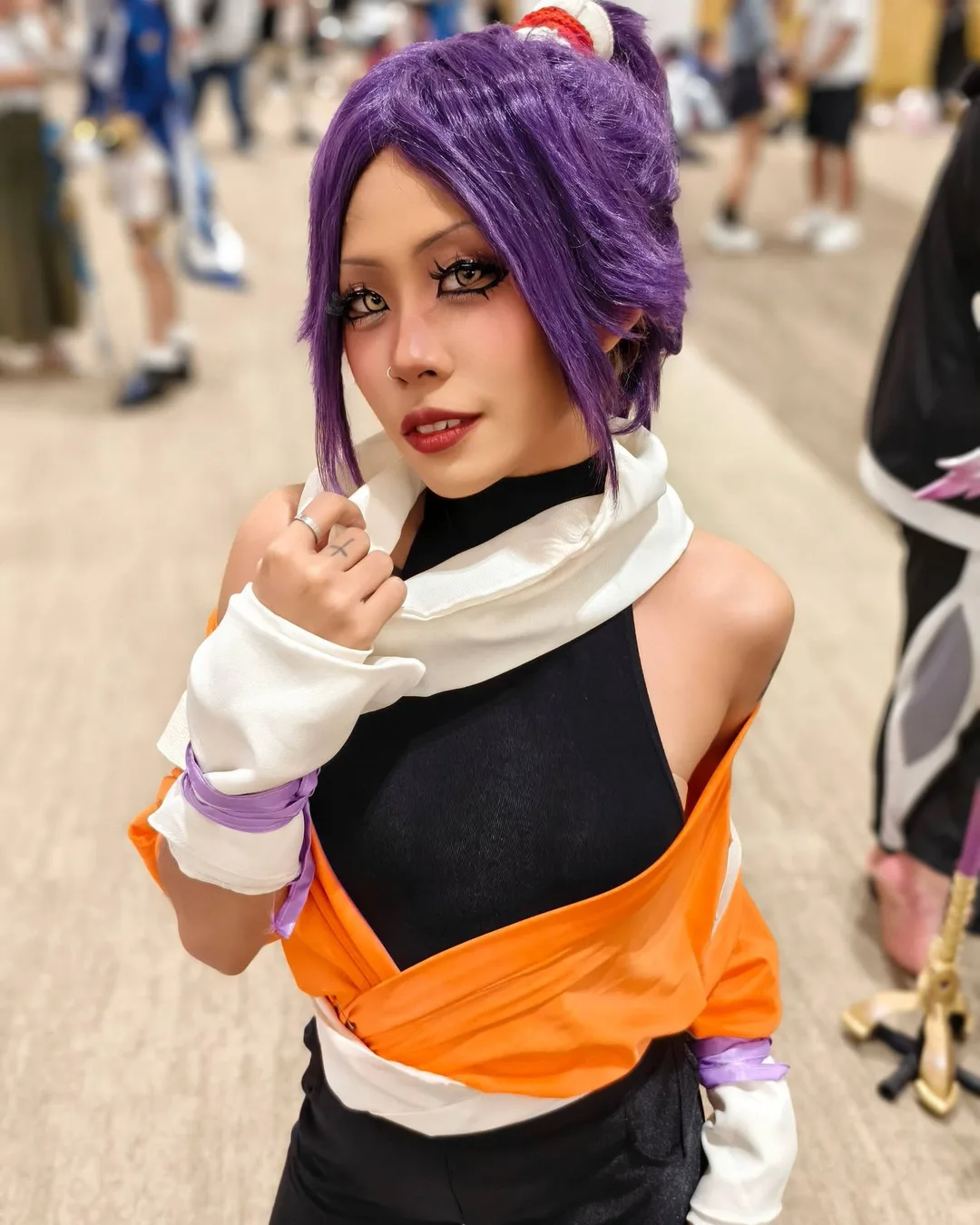 คอสเพลเยอร์แต่งกายเป็น Yoruichi Shihouin จาก Bleach ด้วยวิกผมสีม่วงและชุดสีส้มดำ โพสท่าในงานอีเวนต์