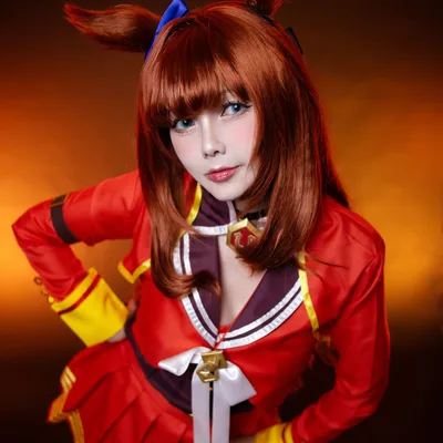 คอสเพลเยอร์แต่งกายเป็น Tokai Teio จาก Uma Musume ในชุดสีแดงทอง โพสท่าโน้มตัวไปข้างหน้าบนพื้นหลังโทนอุ่น