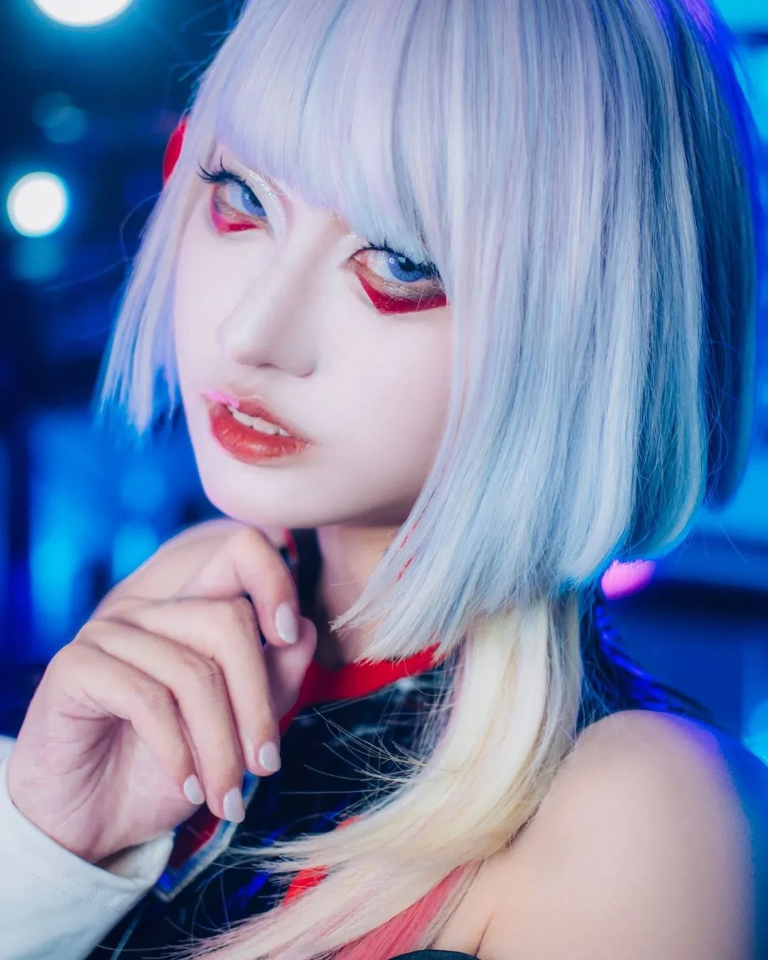 คอสเพลเยอร์แต่งเป็น Lucy จาก Cyberpunk: Edgerunners สวมวิกผมบ็อบสีฟ้าและแต่งตาโทนแดง โพสท่าหน้าแสงไฟนีออนสีน้ำเงิน