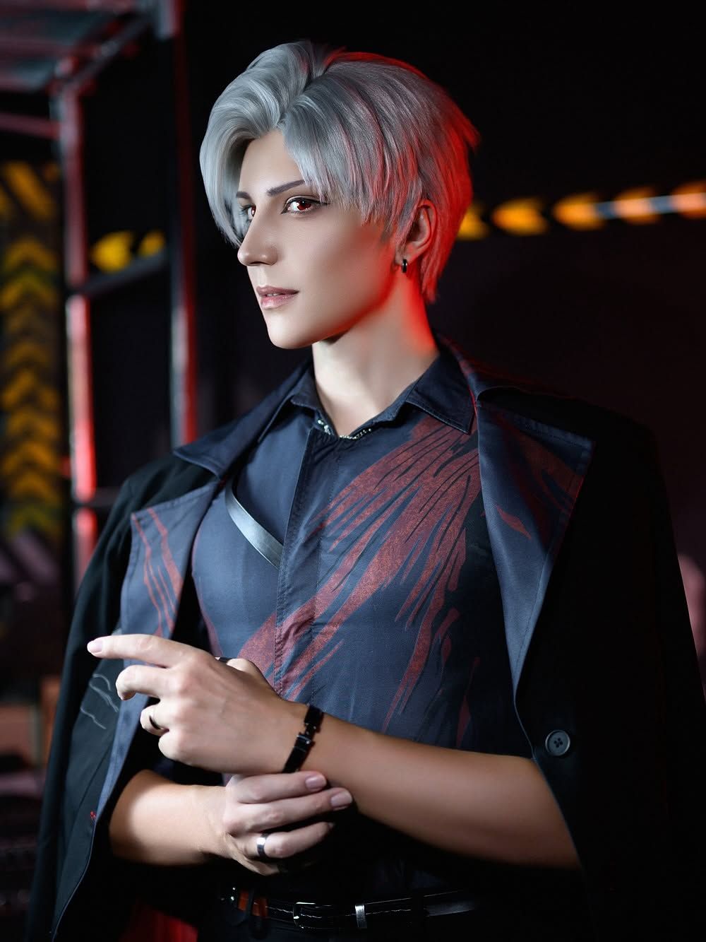 คอสเพลเยอร์แต่งกายเป็น Sylus จาก Love and Deepspace ไว้ผมสั้นสีเงิน โพสท่าในเสื้อเชิ้ตสีดำและเสื้อโค้ตพาดไหล่