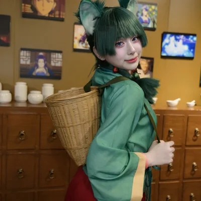 คอสเพลเยอร์แต่งกายเป็น Maomao จาก The Apothecary Diaries สวมหูแมวและสะพายตะกร้าสาน ยืนอยู่หน้าตู้ลิ้นชักยาจีน