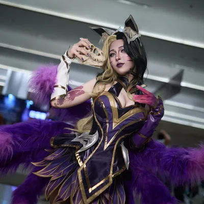 คอสเพลเยอร์ในชุด Coven Ahri โพสท่าถือหน้ากากกะโหลกสัตว์พร้อมหางฟูสีม่วงในงานจัดแสดงในร่ม