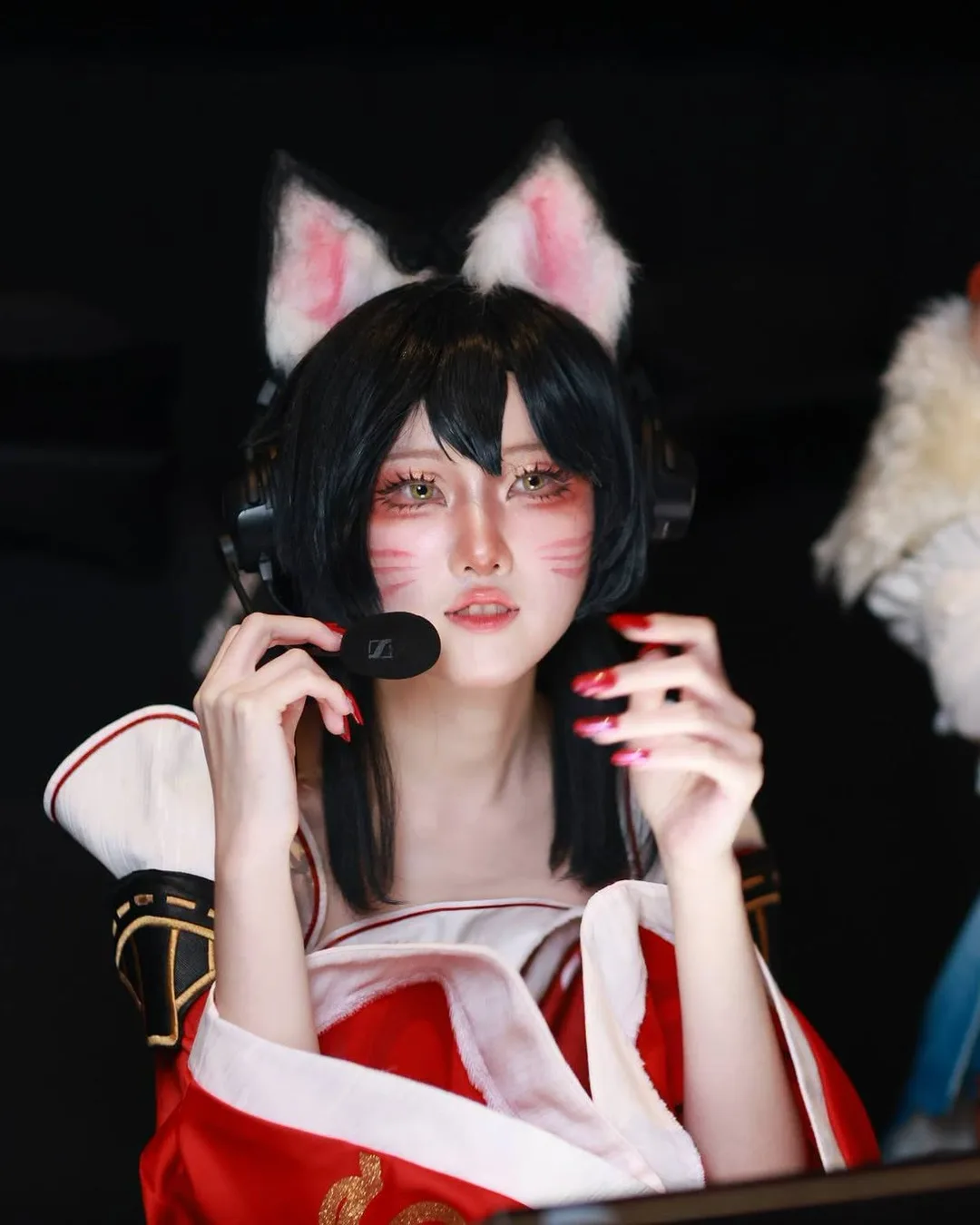 คอสเพลเยอร์ในชุด Ahri สวมหูจิ้งจอกและชุดหูฟัง กำลังปรับไมโครโฟนขณะนั่งอยู่ที่โต๊ะเล่นเกม