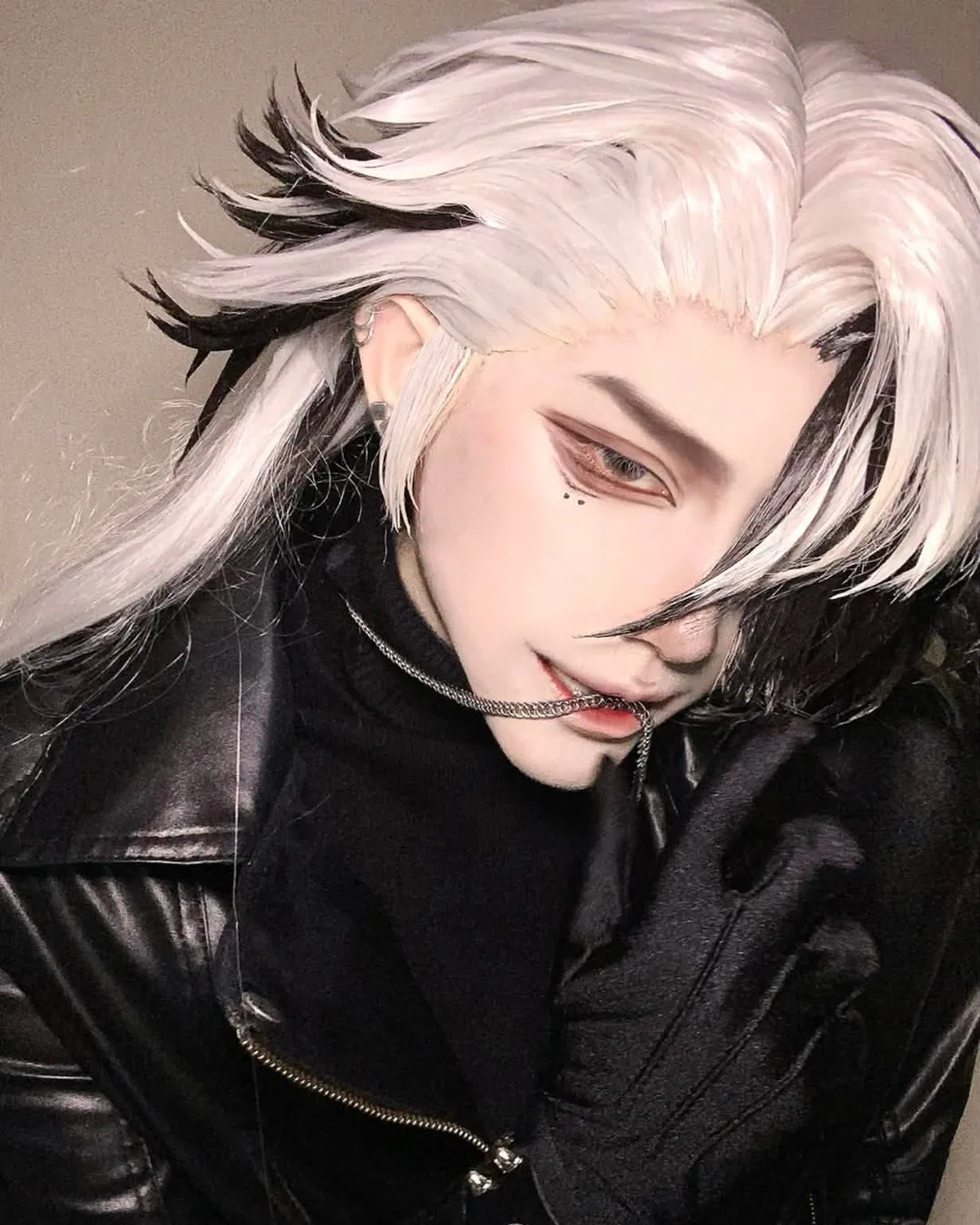คอสเพลเยอร์ผมสีขาวแซมดำและแต่งตาคมเข้ม สวมแจ็กเก็ตหนังสีดำและคาบสายโซ่สีเงินไว้ในปาก