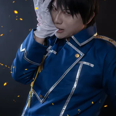 คอสเพลเยอร์แต่งกายเป็น Roy Mustang จาก Fullmetal Alchemist สวมเครื่องแบบทหารสีน้ำเงินและกัดถุงมือสีขาวท่ามกลางประกายไฟ