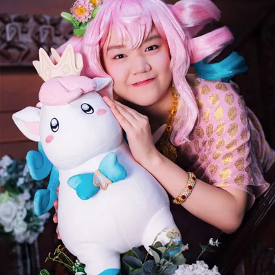 คอสเพลเยอร์ผมสีชมพูยิ้มหวานขณะกอดตุ๊กตาการ์ตูนสีขาวตัวใหญ่ข้างราวบันไดไม้ที่ประดับด้วยดอกไม้