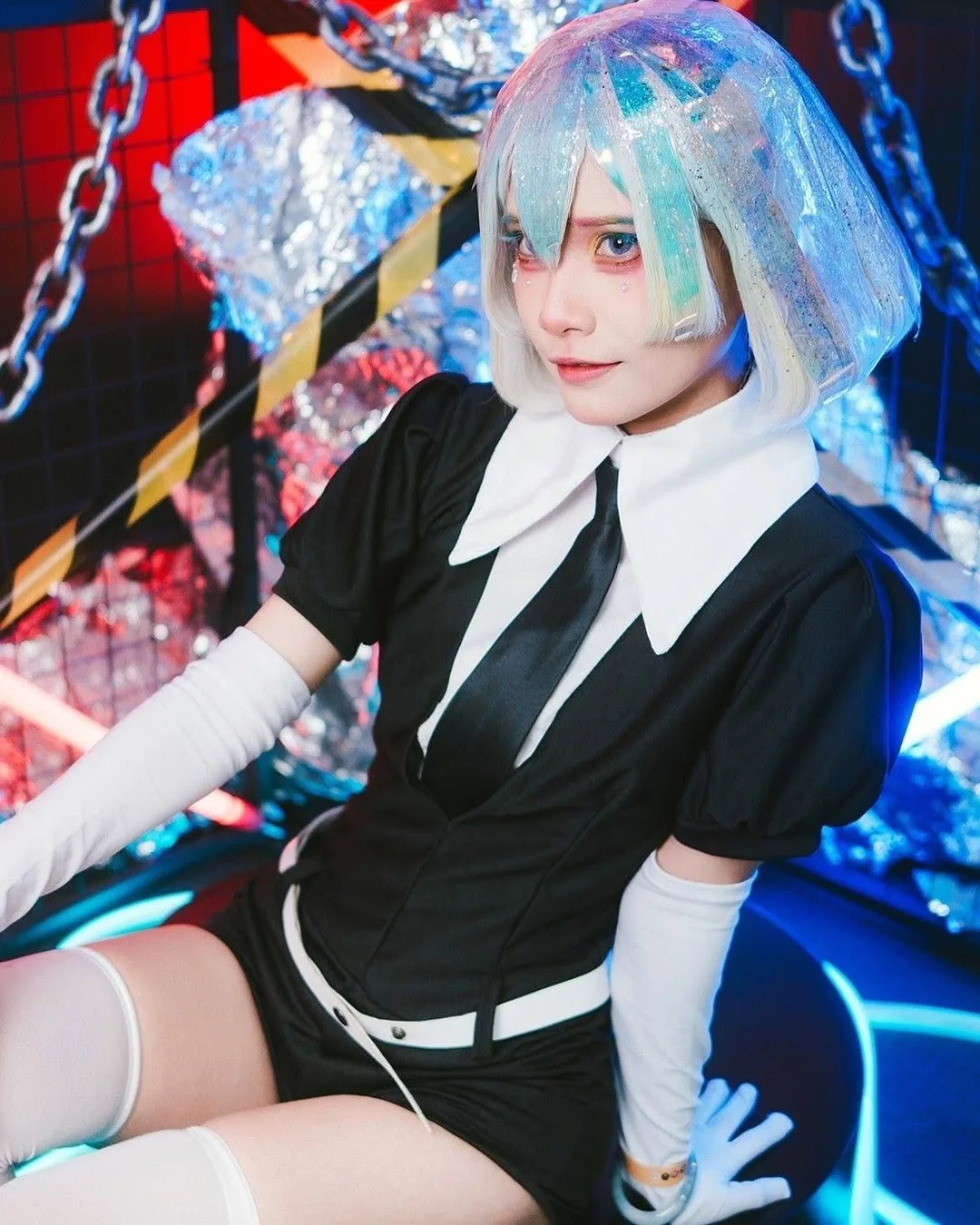 คอสเพลเยอร์ในชุดตัวละคร Diamond จาก Land of the Lustrous นั่งอยู่ในสตูดิโอที่ประดับไฟนีออนและโซ่
