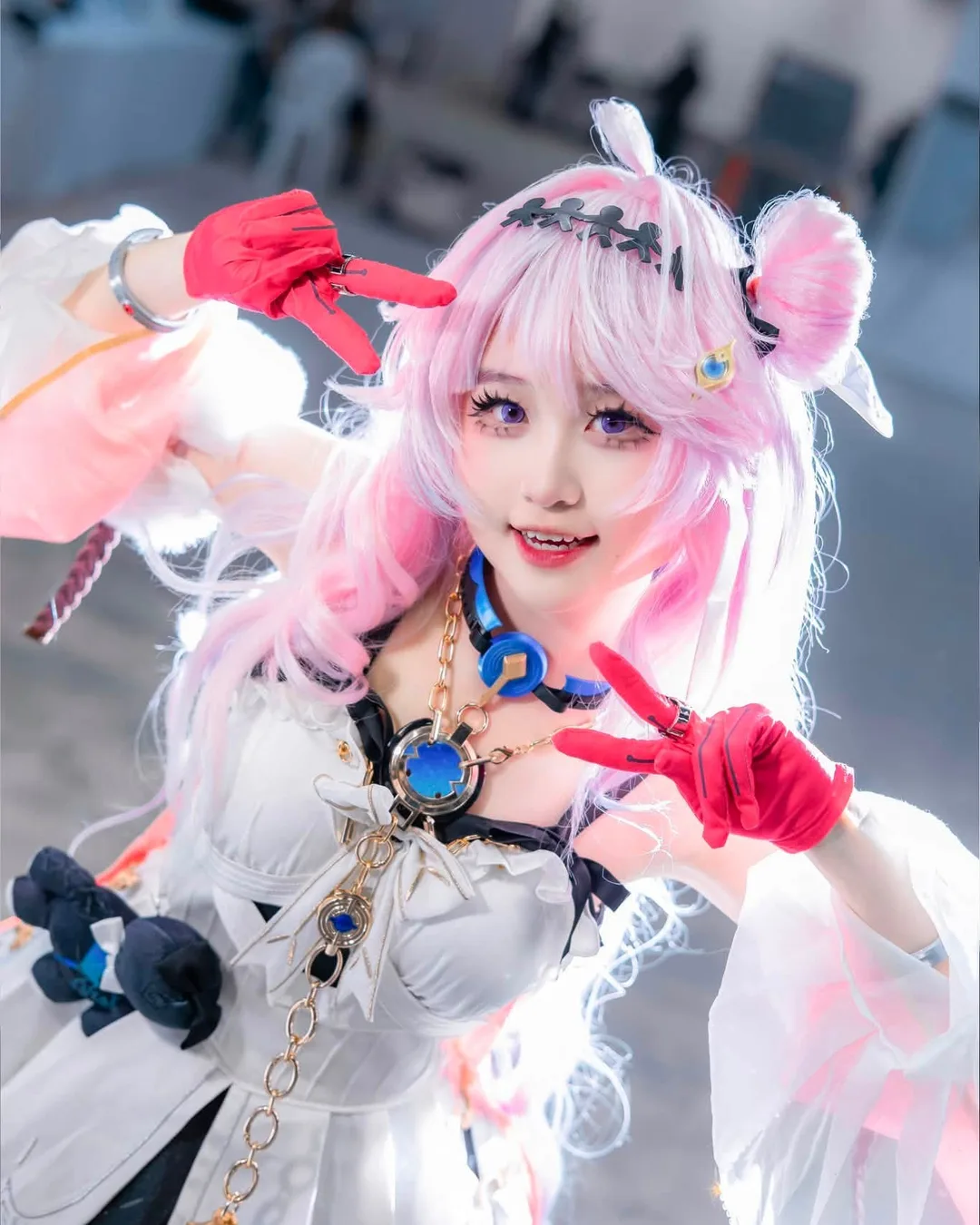 คอสเพลเยอร์ในชุด March 7th จาก Honkai: Star Rail โพสท่าชูสองนิ้วอย่างสดใสในงานอีเวนต์ในร่ม