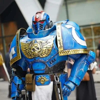 คอสเพลเยอร์ในชุดเกราะพาวเวอร์อาร์เมอร์ Warhammer 40,000 Ultramarine สีน้ำเงินทองยืนอยู่กลางแจ้งในงานกิจกรรม