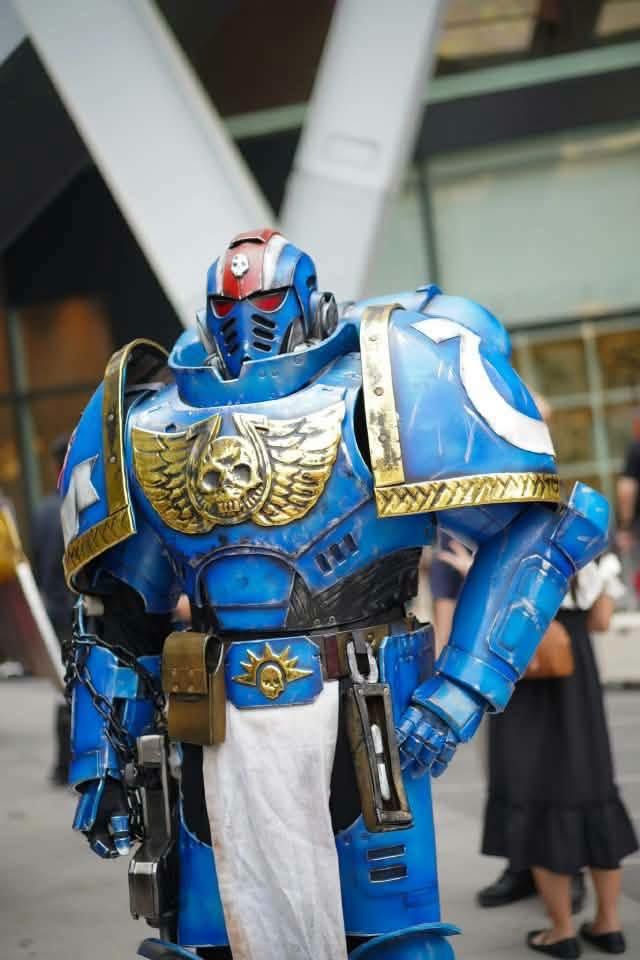 คอสเพลเยอร์ในชุดเกราะพาวเวอร์อาร์เมอร์ Warhammer 40,000 Ultramarine สีน้ำเงินทองยืนอยู่กลางแจ้งในงานกิจกรรม