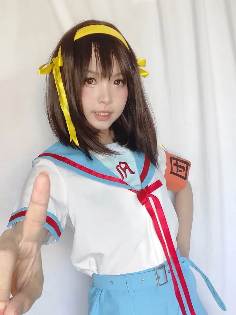 คอสเพลเยอร์แต่งกายเป็น Haruhi Suzumiya ในชุดกะลาสีสีฟ้าขาวชี้นิ้วมาทางกล้องหน้าฉากหลังสีขาว