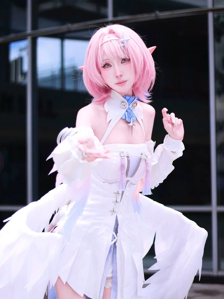 คอสเพลเยอร์ผมสีชมพูติดหูเอลฟ์แต่งชุด Elysia สีขาวติดปีก ยื่นมือข้างหนึ่งมาข้างหน้าขณะโพสท่ากลางแจ้ง