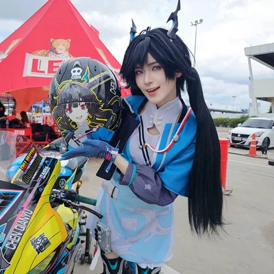 คอสเพลเยอร์ที่มีเขาและมัดผมแกละสีดำยืนโพสท่าข้างมอเตอร์ไซค์ พร้อมถือหมวกกันน็อกลายตัวละครอนิเมะ
