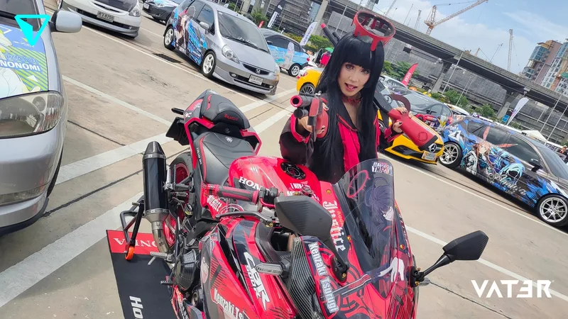 คอสเพลเยอร์ถือปืนของเล่นโพสท่าอยู่ด้านหลังรถจักรยานยนต์ Honda สีแดงลายอนิเมะในงานแสดงอิตาฉะกลางแจ้ง