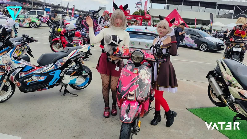 คอสเพลเยอร์สองคนในชุดอนิเมะติดหูสัตว์โพสท่าข้างสกู๊ตเตอร์ลายอนิเมะสีชมพูในงานจัดแสดงรถอิตาฉะกลางแจ้ง