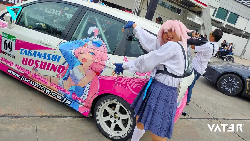 คอสเพลเยอร์วิกผมสีชมพูโพสท่าข้างรถแข่งอิตาฉะลายตัวการ์ตูน Takanashi Hoshino ในลานกิจกรรมกลางแจ้ง