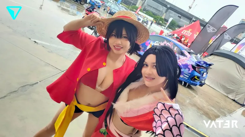 หญิงสาวสองคนยิ้มแย้มขณะคอสเพลย์เป็นลูฟี่และโบอา แฮนค็อก จาก One Piece ในงานกลางแจ้งที่มีรถแต่งอยู่ด้านหลัง