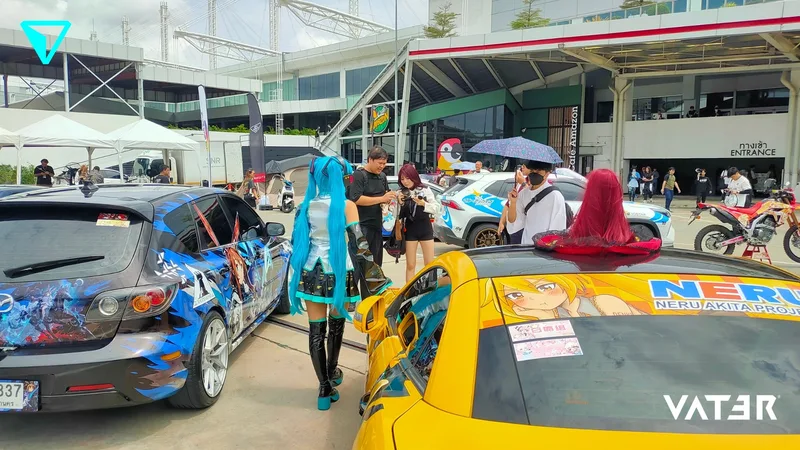 เหล่าเลเยอร์และผู้ร่วมงานเดินผ่านรถแต่งลายอนิเมะหรืออิตาฉะที่จอดอยู่ด้านนอกสถานที่จัดงาน