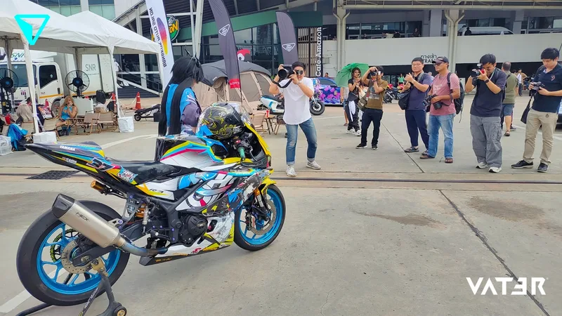 ช่างภาพกำลังถ่ายรูปคอสเพลเยอร์ที่ยืนอยู่หลังมอเตอร์ไซค์สปอร์ตลายอนิเมะสีสันสดใสในงานกลางแจ้ง