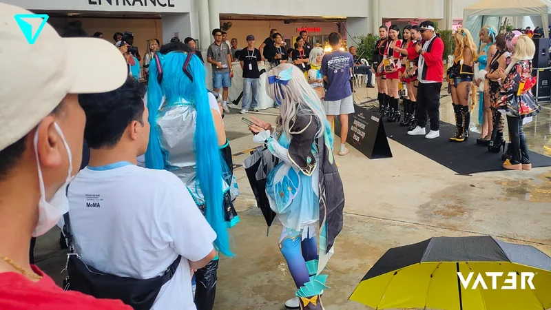 คอสเพลเยอร์ในชุดอนิเมะสีสันสดใสและผู้เข้าร่วมงานรวมตัวกันบริเวณหน้าทางเข้าสถานที่จัดงานใกล้กับกลุ่มพิธีกรและนางแบบ