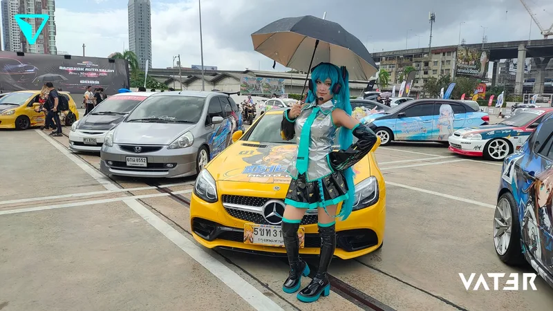 คอสเพลเยอร์ในชุด Hatsune Miku ถือร่มโพสท่าอยู่หน้ารถ Mercedes-Benz สีเหลืองในงานจัดแสดงรถยนต์กลางแจ้ง